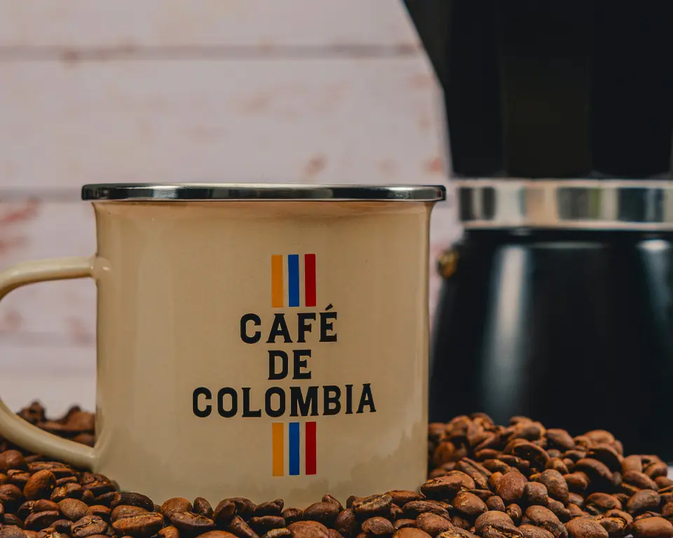 Una taza de café junto a una cafetera moka y granos